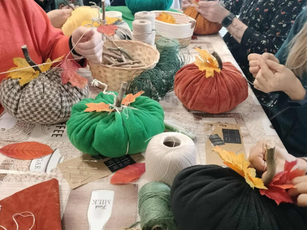 Na stole znajduje się dużo dyń zrobionych z tkaniny oraz sznurków. Każda dynia ma indywidualny kolor i wygląd.