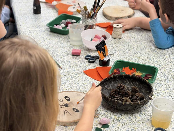 Dzieci robią zwierzątka na plastrze drewna.