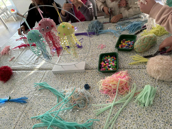 Widok na stół z meduzami zrobionymi z kreatywnych drucików. Robótki są bardzo kolorowe
