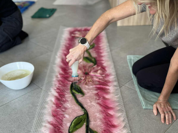 Uczestniczka jest w takcie tworzenia szala szesankowego. Szal jest różowy z motywem kwiatowym.
